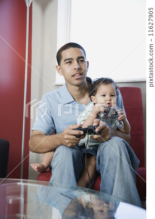 Young African father playing video games with baby on lap 11627905