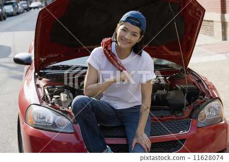 Asian woman sitting next to open car hood 11628074