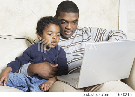 African American father and young son with laptop on sofa 11628216