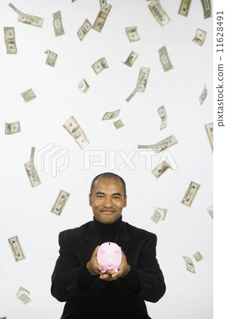 Money raining down on Asian businessman holding piggy bank 11628491