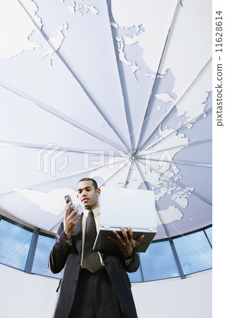 Low angle view of businessman with cell phone and laptop 11628614