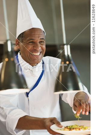 Mixed Race male chef garnishing plate of food Mixed Race male chef garnishing plate of food 11628649