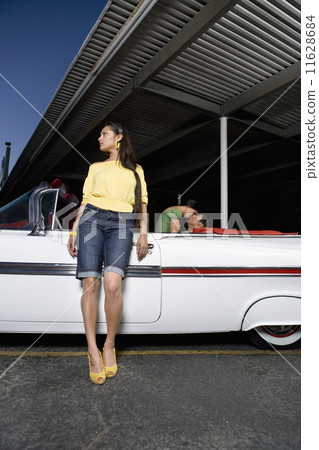 Hispanic woman leaning on convertible 11628684