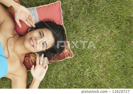 Young woman lying outside listening to music 11628727