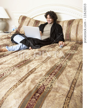Hispanic man typing on laptop in bed 11628833