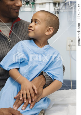 African boy in hospital gown sitting on father's lap 11628936