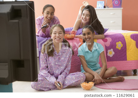 Four girls in bedroom watching television and eating snacks 11629061