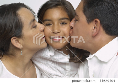 Hispanic parents kissing daughter's cheeks 11629104