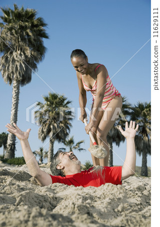 Mixed Race woman burying husband in sand 11629111