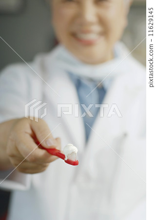 Female dentist holding out toothbrush with toothpaste Female dentist holding out toothbrush with toothpaste 11629145