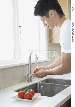 Asian man washing tomatoes in kitchen Asian man washing tomatoes in kitchen 11629239