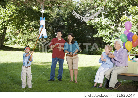 Family watching Hispanic boy hitting pinata at birthday party 11629247