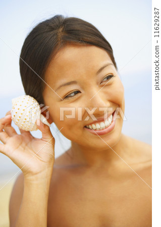 Asian woman listening to seashell 11629287