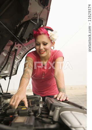 Tattooed Hispanic woman looking under car hood Tattooed Hispanic woman looking under car hood 11629374