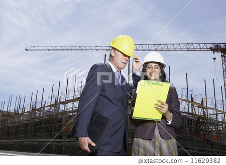 Businesswoman and businessman wearing hard hats at construction site Businesswoman and businessman wearing hard hats at construction site 11629382