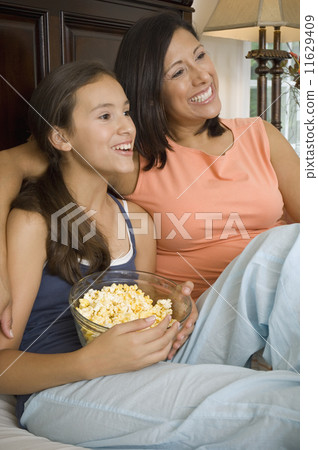 Hispanic mother and daughter watching television 11629409