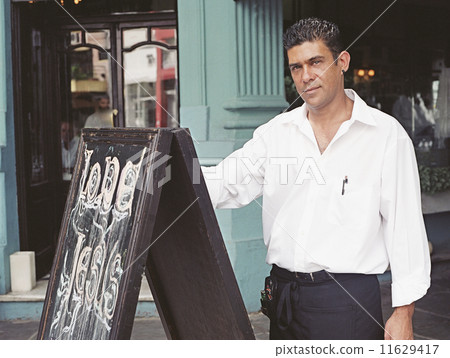 Hispanic waiter next to chalkboard in front of restaurant 11629417