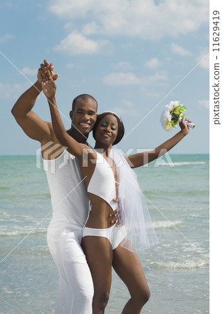 African bride and groom hugging at beach 11629419