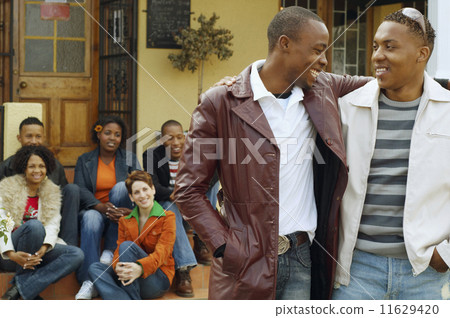 African men hugging with friends in background African men hugging with friends in background 11629420