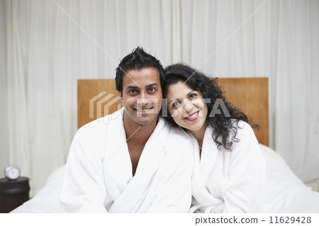 Middle Eastern couple smiling in bathrobes on bed 11629428