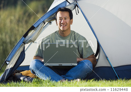 Portrait of man on laptop outside of tent Portrait of man on laptop outside of tent 11629448
