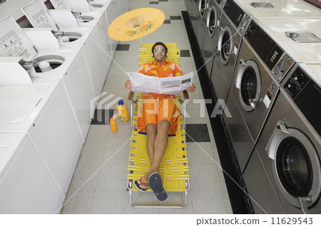 Man with lounge chair and umbrella reading newspaper in laundromat 11629543