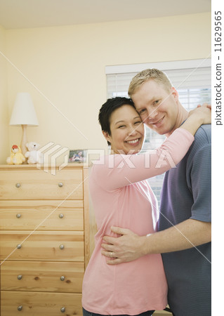 Pregnant couple hugging indoors  11629565