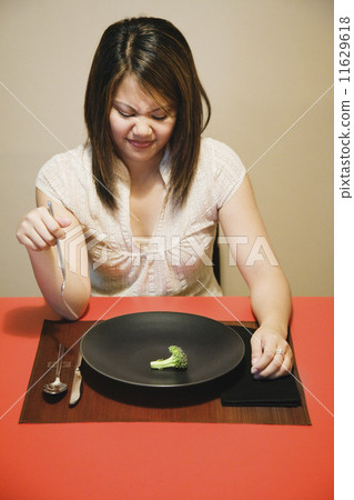 Asian woman with one piece of broccoli on plate 11629618