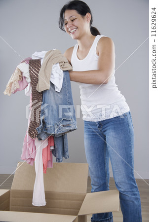Young woman piling clothes into a cardboard box Young woman piling clothes into a cardboard box 11629624
