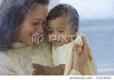 Hispanic mother holding baby behind rainy glass Hispanic mother holding baby behind rainy glass 11629682
