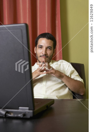 Hispanic man sitting at desk with laptop 11629849