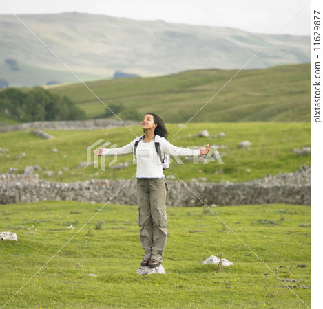 Young woman standing on a rock with her arms outstretched in rural location 11629877