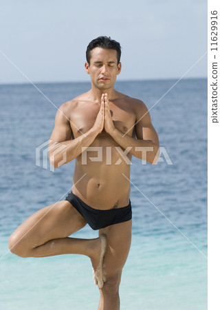Hispanic man practicing yoga at beach 11629916