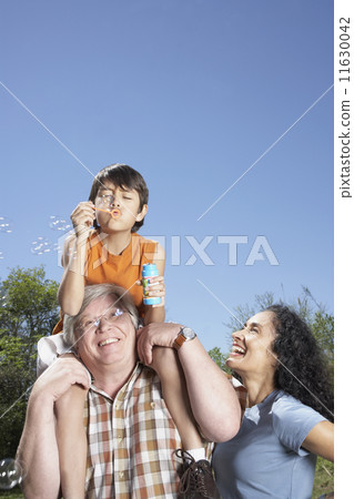 Hispanic grandparents and grandson blowing bubbles outdoors 11630042