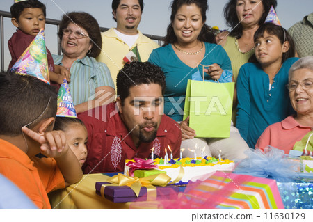 Hispanic man blowing out candles on birthday cake with family 11630129
