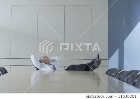 Senior Asian businessman sitting at head of conference table with his feet up 11630201