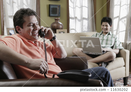 Hispanic father and son relaxing in livingroom 11630202