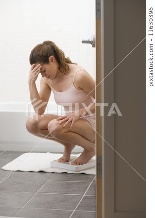 Hispanic woman frowning on bathroom scale Hispanic woman frowning on bathroom scale 11630396
