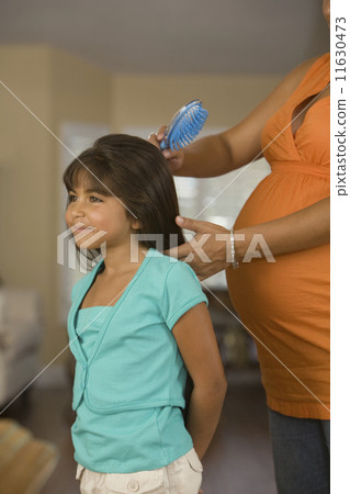 Pregnant Hispanic mother brushing daughter's hair Pregnant Hispanic mother brushing daughter's hair 11630473