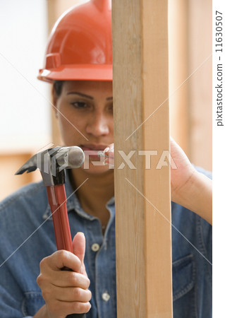 Female construction worker hammering nail into framework Female construction worker hammering nail into framework 11630507