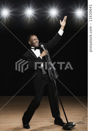 African American man in tuxedo singing into microphone onstage 11630641
