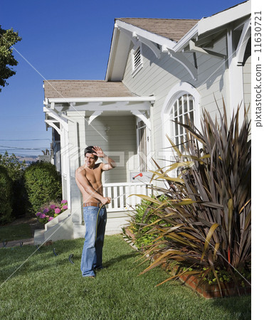 Bare-chested Hispanic man watering plants 11630721