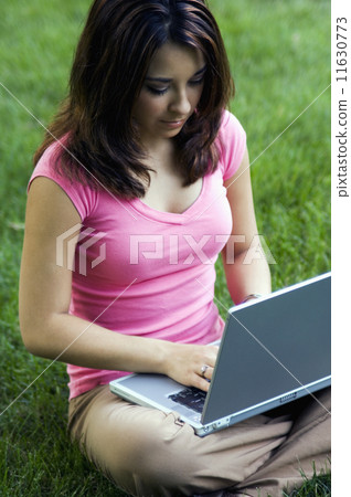 Young woman typing on laptop in grass Young woman typing on laptop in grass 11630773