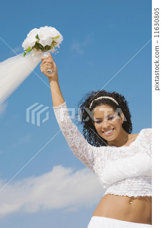 Hispanic bride holding bouquet over head 11630805
