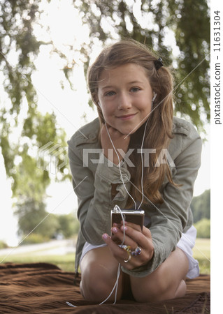 Teenage girl listening to mp3 player on blanket outdoors Teenage girl listening to mp3 player on blanket outdoors 11631304