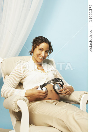 Pregnant Mixed Race woman holding headphones on belly Pregnant Mixed Race woman holding headphones on belly 11631373