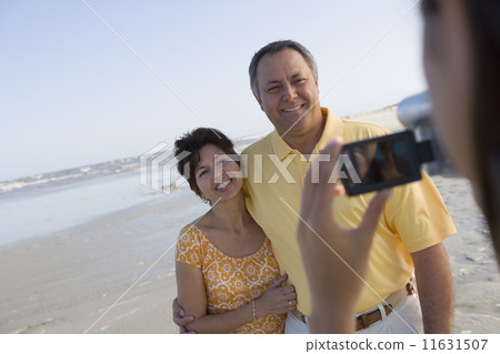 Hispanic couple being video recorded at beach 11631507