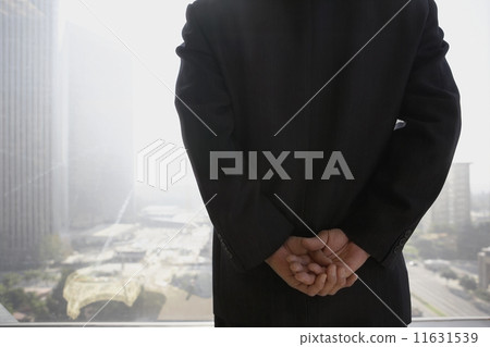 Businessman with hands clasped behind his back in front of window  11631539