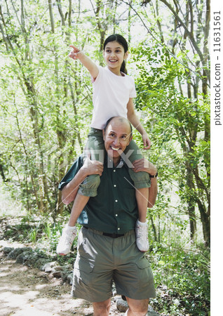 Hispanic grandfather holding granddaughter on shoulders in woods 11631561