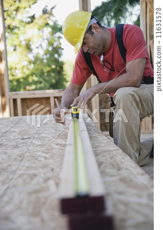Mixed Race male construction worker measuring wood Mixed Race male construction worker measuring wood 11631578